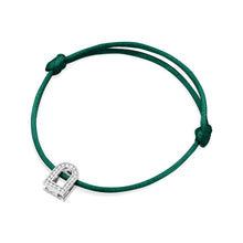 Load image into Gallery viewer, The L'Arc Voyage Charm PM bracelet features a slender silk cord in green, elegantly tied in a simple knot. It is adorned with a small charm made of 18k white gold and encrusted with Galerie diamonds, shaped like a horseshoe, showcasing the timeless craftsmanship of Paris Atelier.
