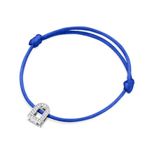 Load image into Gallery viewer, A silk cord bracelet in blue, showcasing the L'Arc Voyage Charm PM, crafted from 18k white gold and adorned with Galerie diamonds, reminiscent of a Paris Atelier creation. The cord elegantly loops with knots at each end against a plain white background.
