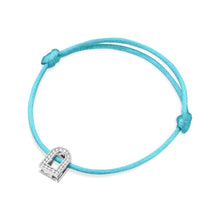 Load image into Gallery viewer, Introducing the L'Arc Voyage Charm PM bracelet from Paris Atelier, featuring a silk cord in vibrant turquoise. At its center is an elegant 18k white gold padlock charm adorned with Galerie diamonds, perfectly highlighted by the simple knots tying the cord.
