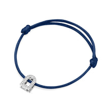 Load image into Gallery viewer, Introducing the L'Arc Voyage Charm PM, an elegant bracelet designed with a sophisticated dark blue silk cord and a lock-shaped charm crafted from 18k white gold. This exquisite piece, meticulously created in the Paris Atelier, features Galerie Diamonds that add a touch of sparkling brilliance. The cord is secured with two knots, offering both simplicity and elegance.
