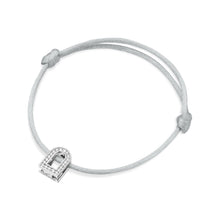 Load image into Gallery viewer, The L'Arc Voyage Charm PM bracelet, featuring an 18k white gold horseshoe-shaped charm embellished with Galerie diamonds, is elegantly displayed on a plain white background. This sophisticated piece from the Paris Atelier collection is set on a thin silk cord with an adjustable knot design.
